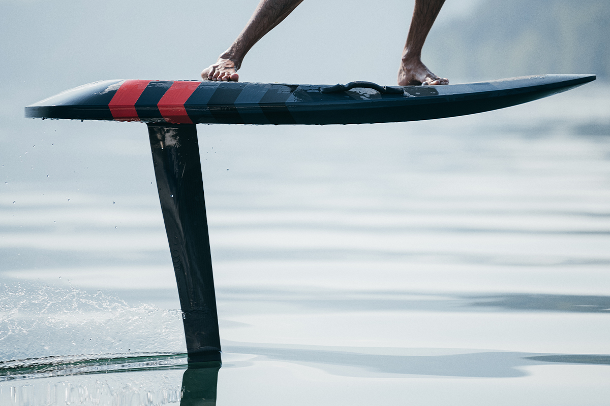 Nahaufnahme eines E-Foils mit rot-schwarzem Board und Tragfluegel ueber der Wasseroberflaeche