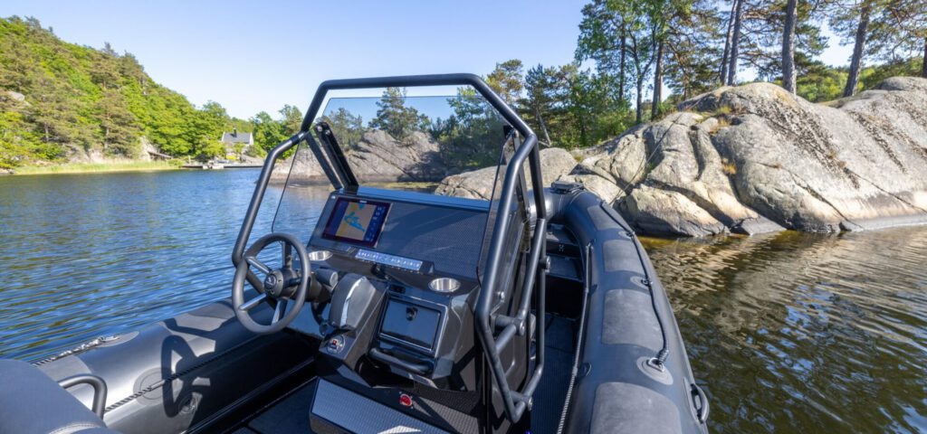 Schwarzes Highfield-RIB mit Steuerstand vor felsiger Kueste und Kiefern