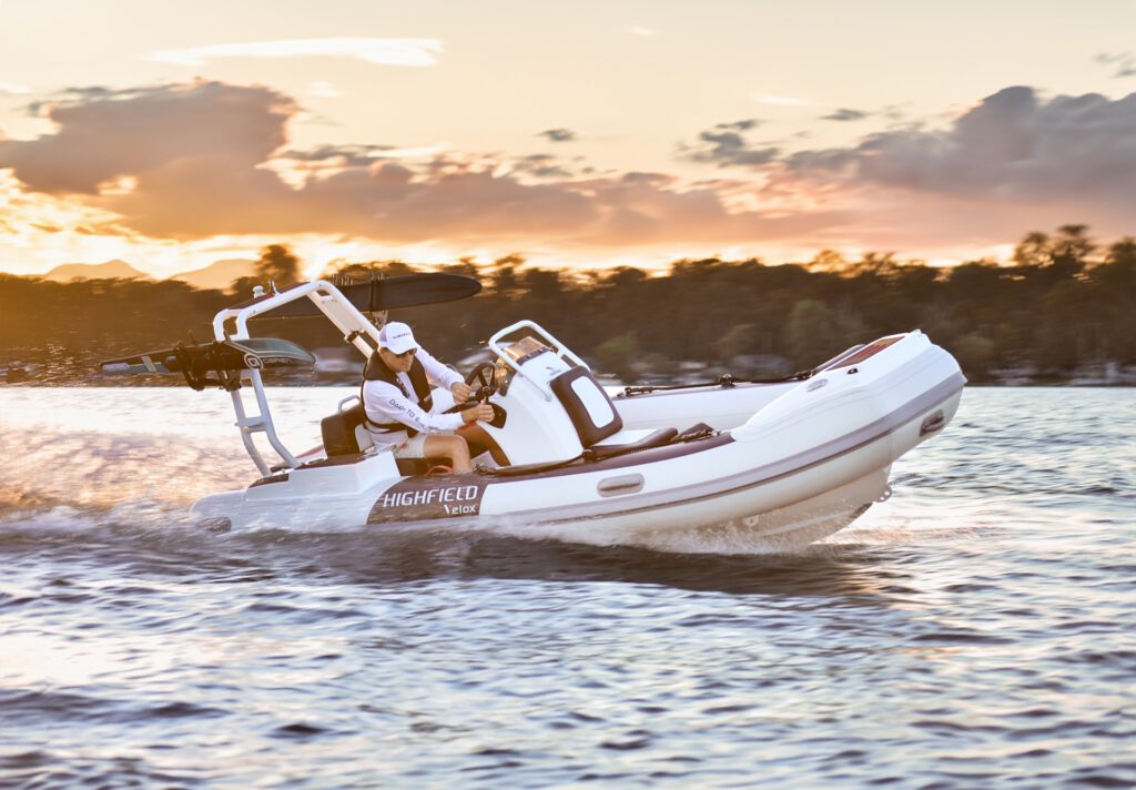 Weisses Schlauchboot mit Festrumpf faehrt bei Sonnenuntergang ueber ruhiges Wasser