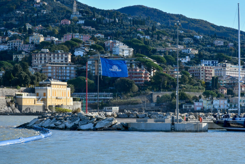 Blick vom Wasser auf Rapallo mit bewaldeten Huegeln und blauer Hafenflagge