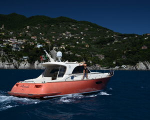 Rote Motoryacht in Fahrt vor der bewaldeten Kueste bei Portofino