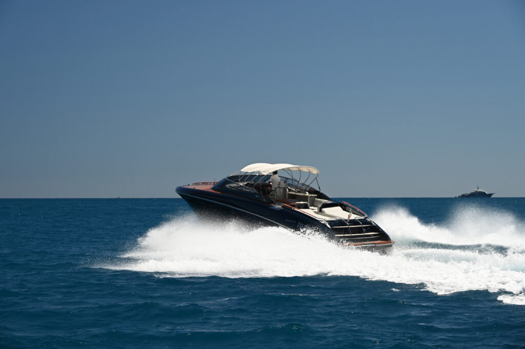 Dunkle Riva Motoryacht in voller Fahrt auf offenem blauen Meer, Luftaufnahme