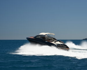 Dunkle Riva Motoryacht in voller Fahrt auf offenem blauen Meer, Luftaufnahme