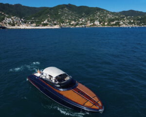 Elegante Motoryacht mit Mahagoni-Rumpf auf blauem Meer vor gruener Kueste