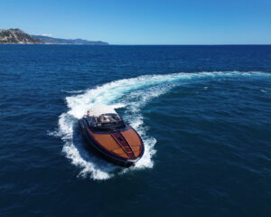 Riva Motoryacht mit Bugwelle in Fahrt auf blauem Meer, Luftaufnahme