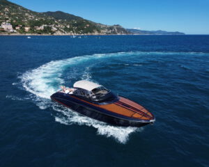 Dunkle Riva Motoryacht mit Mahagoni-Deck auf tiefblauem Meer vor der Kueste, Luftaufnahme