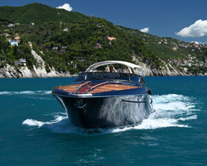 Bugansicht einer Riva Motoryacht mit Mahagoni-Deck in Fahrt vor tuerkisem Wasser und Kueste