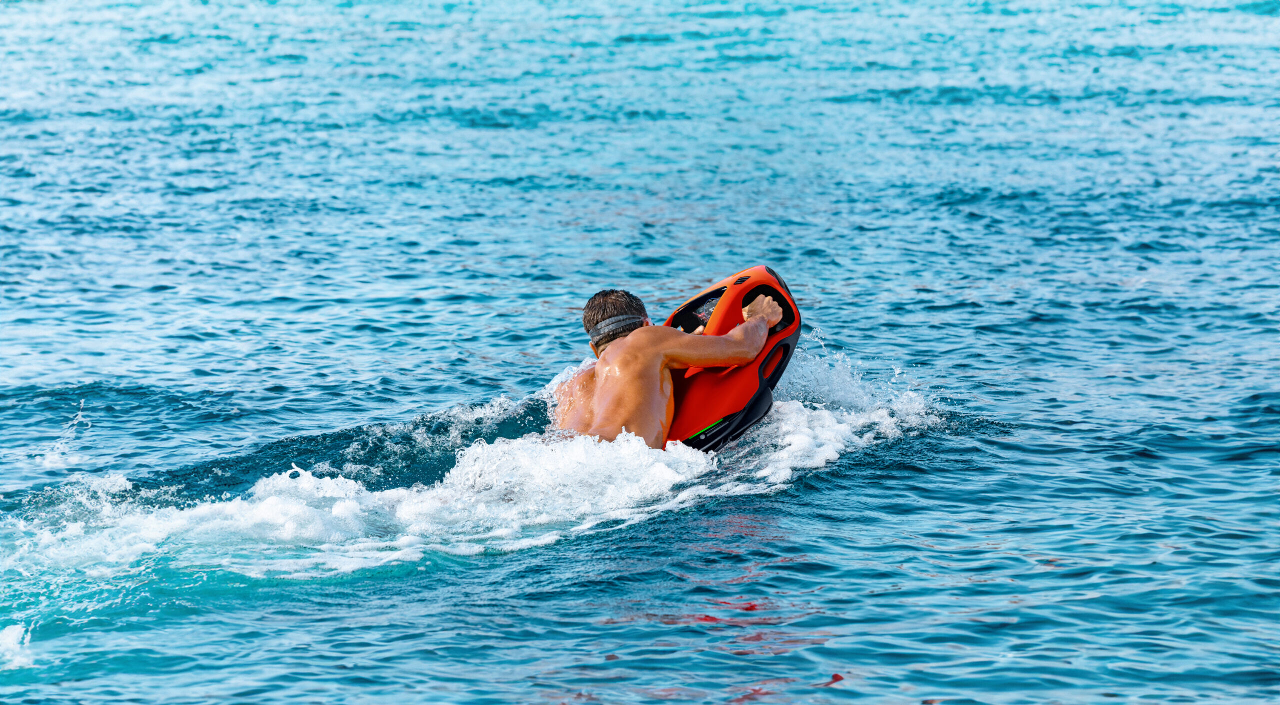 Mann gleitet mit orangefarbenem Seabob über die Wasseroberfläche im offenen Meer