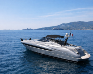 Silberne Riva-Motoryacht vor Anker auf blauem Wasser vor bergiger Kueste